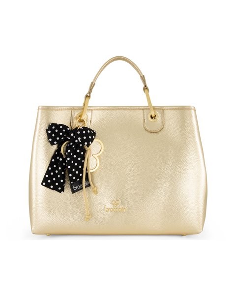 The Beth Metallic Charm Tote Bag: a champagne-gold tote with a black polka-dot ribbon and daisy charm on its handle.